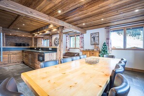 A wooden interior with a dining table, chairs, a kitchen area, and a Christmas tree.