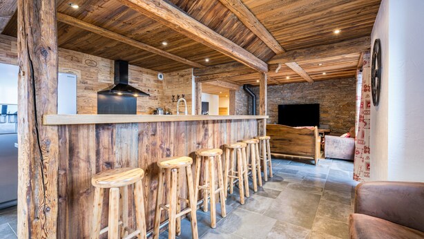 A rustic interior with a wooden bar, stools, stone walls, and a fireplace. - Apartment "La Source" with Mountain Views, Private Terrace, and Wi-Fi (Valloire)