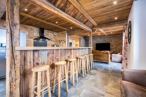 A rustic interior with a wooden bar, stools, stone walls, and a fireplace.