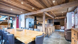 A rustic interior with a wooden dining table, chairs, a kitchen area, and a fireplace. - Apartment "La Source" with Mountain Views, Private Terrace, and Wi-Fi (Valloire)