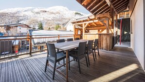 A wooden deck with a table and chairs, overlooking a snowy mountain landscape. - Apartment "La Source" with Mountain Views, Private Terrace, and Wi-Fi (Valloire)