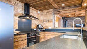 A modern kitchen with wooden accents, stainless steel appliances, and a stone backsplash. - Apartment "La Source" with Mountain Views, Private Terrace, and Wi-Fi (Valloire)