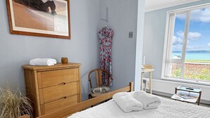 Un dormitorio con una cama grande, un aparador de madera, una silla y una ventana con vista al océano.