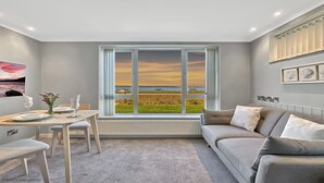 Una sala de estar moderna con un amplio ventanal que ofrece una vista panorámica del atardecer sobre una playa.