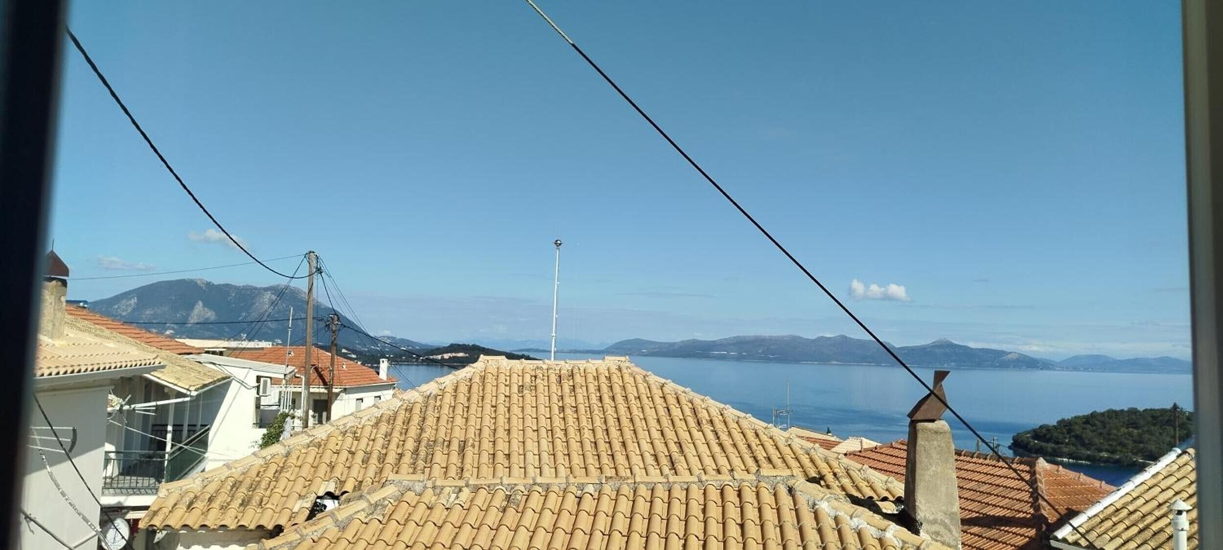 Een kustgezicht met terracottadakpannen, een heldere lucht en verre bergen.