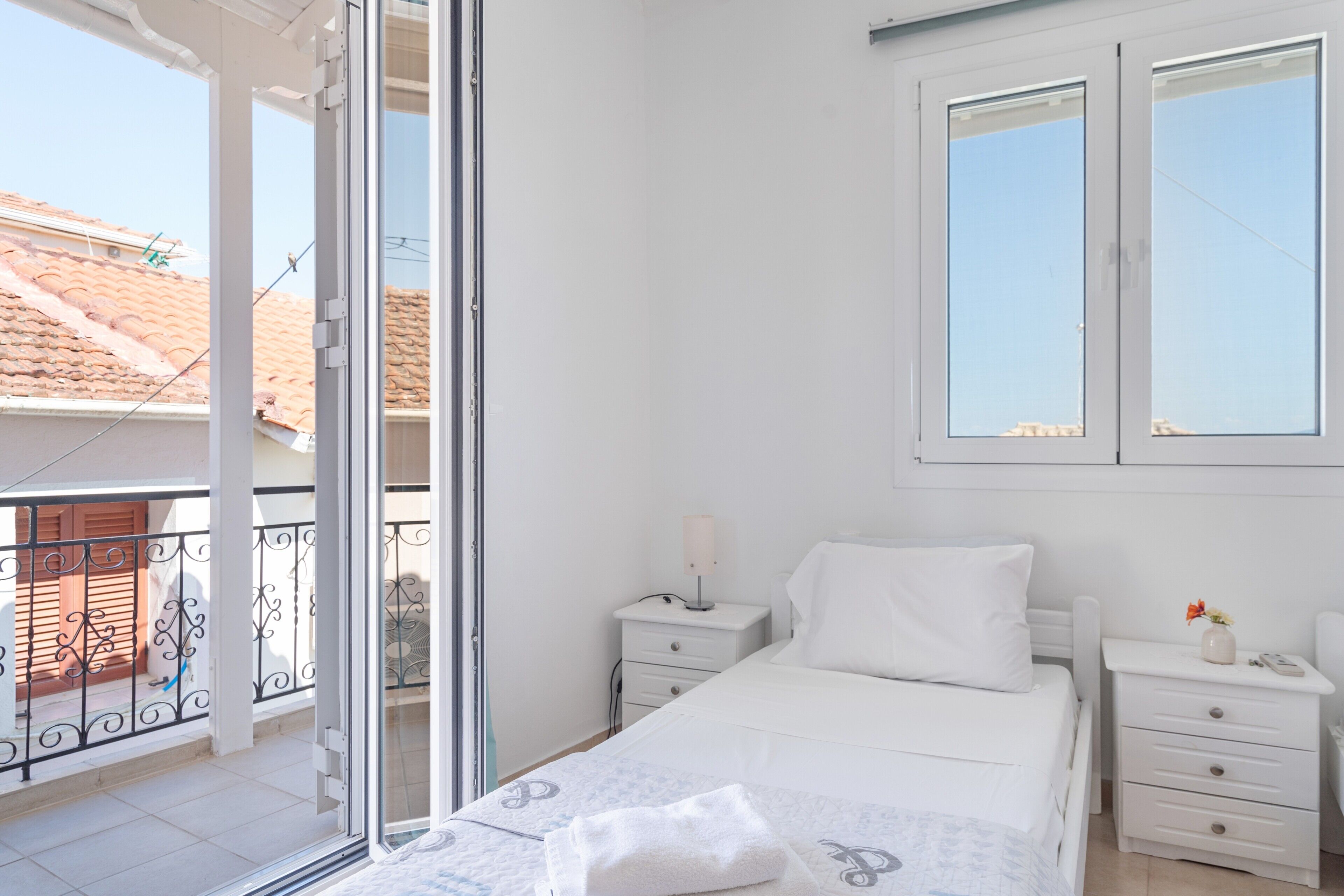 Een slaapkamer met een bed, nachtkastje, raam en balkon.