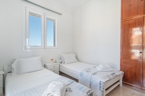 A bedroom with two beds, a wooden wardrobe, a window, and a bedside table with a lamp.
