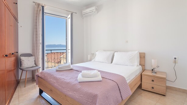 A bedroom with a bed, bedside table, chair, and a view of the outdoors.