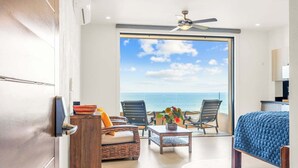 Ein modernes Zimmer mit großem Fenster, einem Bett, einem Deckenventilator und Blick auf den Ozean.