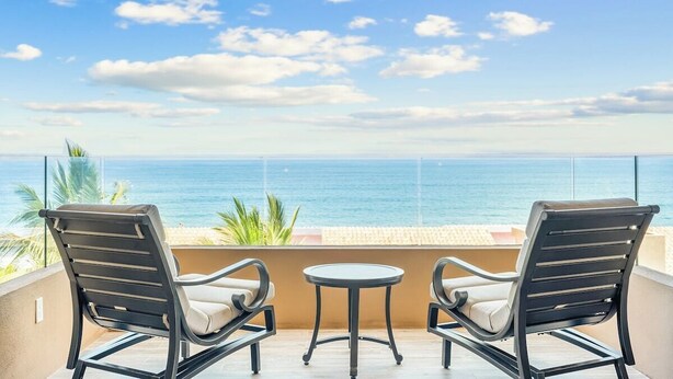Ein Balkon mit zwei Stühlen und einem kleinen Tisch, mit Blick auf einen Strand und den Ozean.