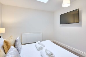 Quarto de hotel com cama, televisão de tela plana na parede, radiador e claraboia.