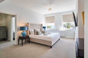 A bedroom with a large bed, a bedside table with a lamp, and a view of the outdoors through a window. - Host Stay Albert House (Weymouth)
