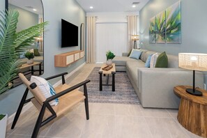 A modern living room with a sofa, a coffee table, a TV mounted on the wall, and a lamp. - Near Theme Parks•Drive•Pvt Pool•Poker Room (Orlando)