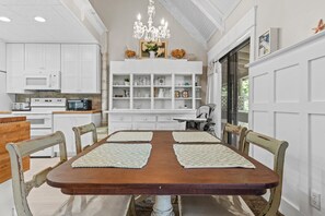 Cozy dining area with a wooden table set for four, surrounded by vintage-style chairs and a shelving unit.