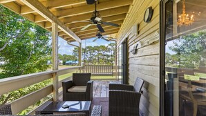 A covered outdoor patio with wicker furniture, a ceiling fan, and a view of the surrounding greenery.