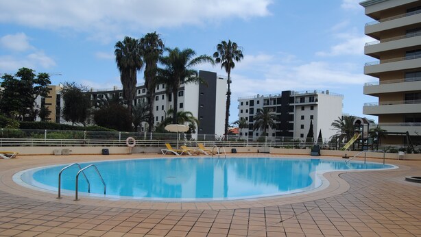 A swimming pool with tiled flooring, surrounded by palm trees and modern buildings. - Aurora Park with swimming pool (Funchal)
