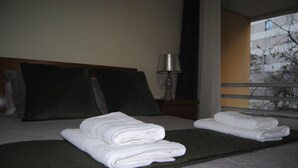 A neatly made bed with folded white towels, a dark green throw blanket, and two dark pillows. - Aurora Park with swimming pool (Funchal)