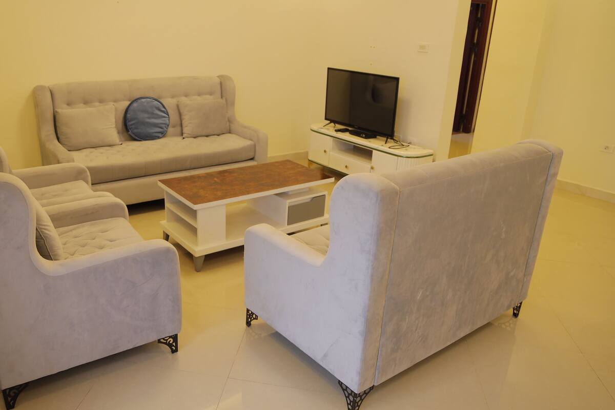 A living room with a sofa, two armchairs, a coffee table, and a TV.