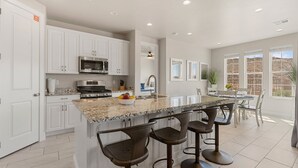 Une cuisine moderne avec des meubles blancs, un plan de travail en granit et un îlot central doté de tabourets de bar.