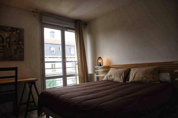 A bedroom with a bed, a desk, and a window.