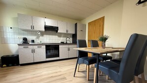 Una cocina moderna con armarios grises, horno empotrado y cafetera. Hay una mesa de comedor con cuatro sillas y un florero con una planta.