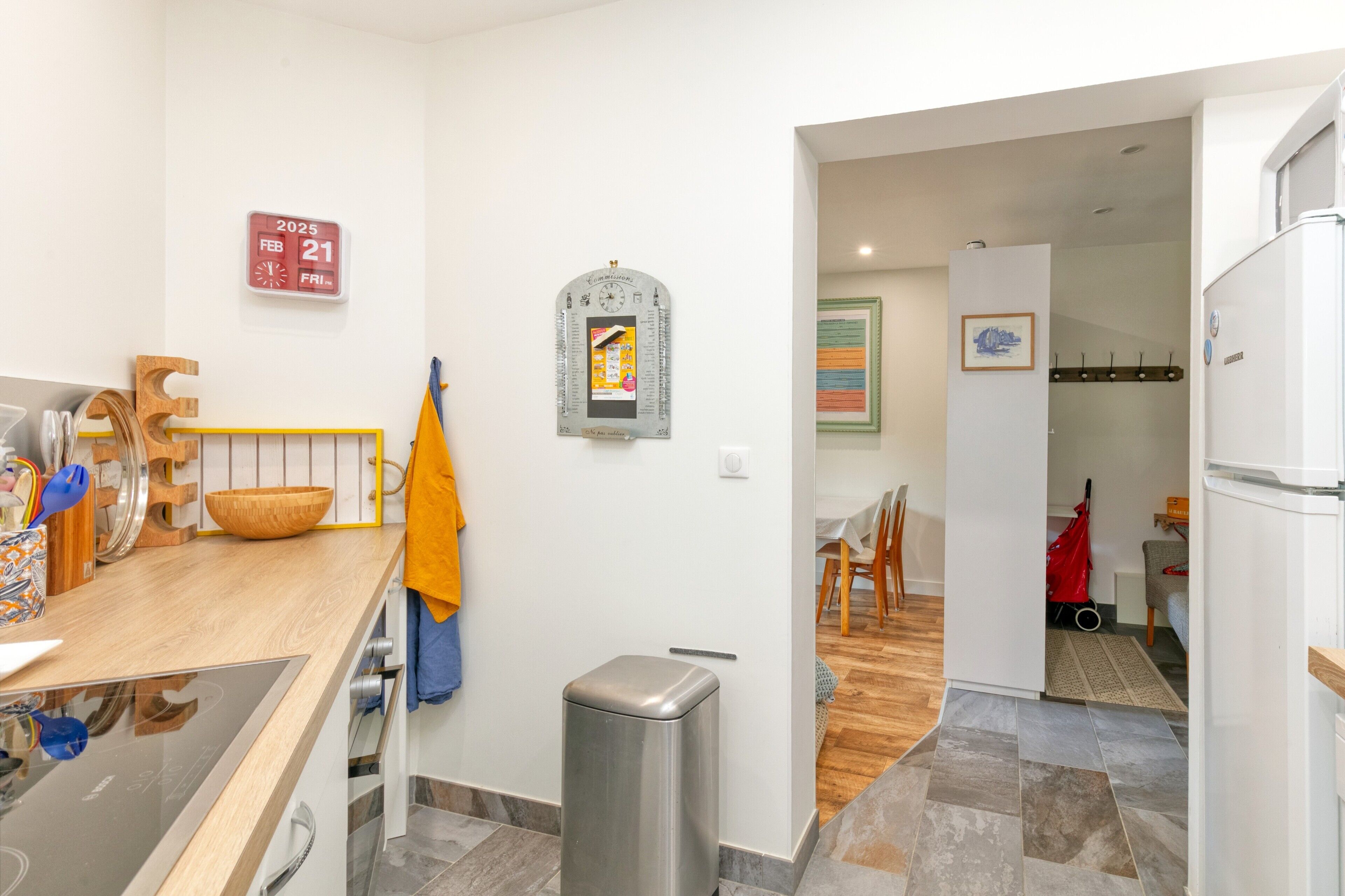 Una cocina moderna con encimera de madera, un cubo de basura de acero inoxidable y un calendario colgado en la pared.