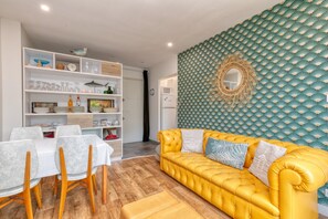 A living room with a yellow sofa, white chairs, a dining table, and a patterned wall.