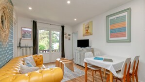 Un salon avec un canapé jaune, une table à manger avec des chaises, un téléviseur et des œuvres d’art accrochées aux murs.