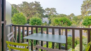 Un balcon avec une table et des chaises, donnant sur un parking et des arbres.