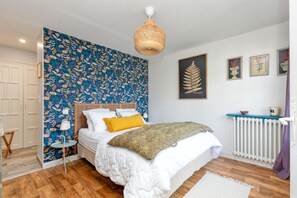 A bedroom with a bed, a wall with floral wallpaper, a hanging light fixture, and a radiator.