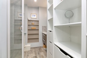 A bathroom with a shower, a toilet, a sink, and a mirror. Shelves are present for storage.