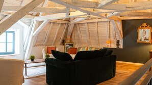 An attic room with exposed wooden beams, a green sofa, a small table with a plant, and a window. - Domaine 'Gîte De L'Abbaye' with Private Pool, Private Terrace and Wi-Fi (Rollainville)