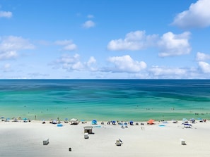 A beach with clear turquoise water, white sand, and a few umbrellas and beach chairs.