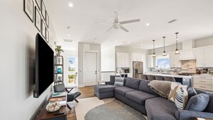 A modern living room with a sectional sofa, a flat-screen TV mounted on the wall, a wooden coffee table, and a decorative plant. - 8 Minute Walk to Beach | Dogs Allowed (Port St. Joe)