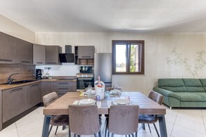 Una cucina moderna con elettrodomestici integrati, una zona pranzo con tavolo e sedie in legno, e un divano verde in un ambiente luminoso.