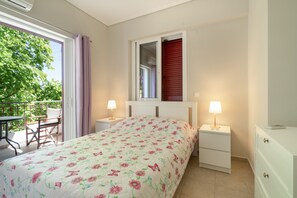 Un dormitorio con cama, mesita de noche, cómoda, ventana con vistas a la vegetación y balcón con mesa y sillas.