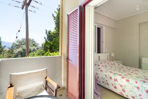Un balcon avec une chaise, un lit recouvert d’une couvre-lit à motifs floraux et une vue sur la verdure et les montagnes.