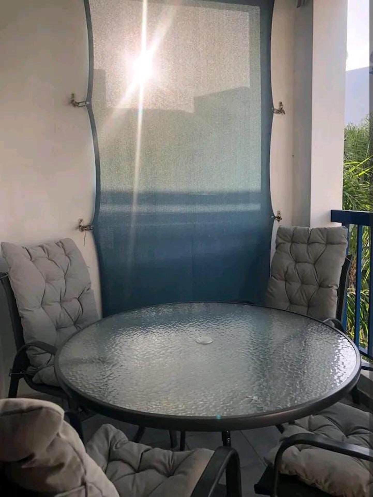 A round glass table with cushioned chairs, a blue wall, and a view of greenery.