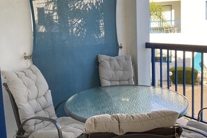 A round glass table with two cushioned chairs, a blue wall, and a balcony with a railing. - Paphos Pool View gem - Cozy 1 bed Apartment (Paphos)