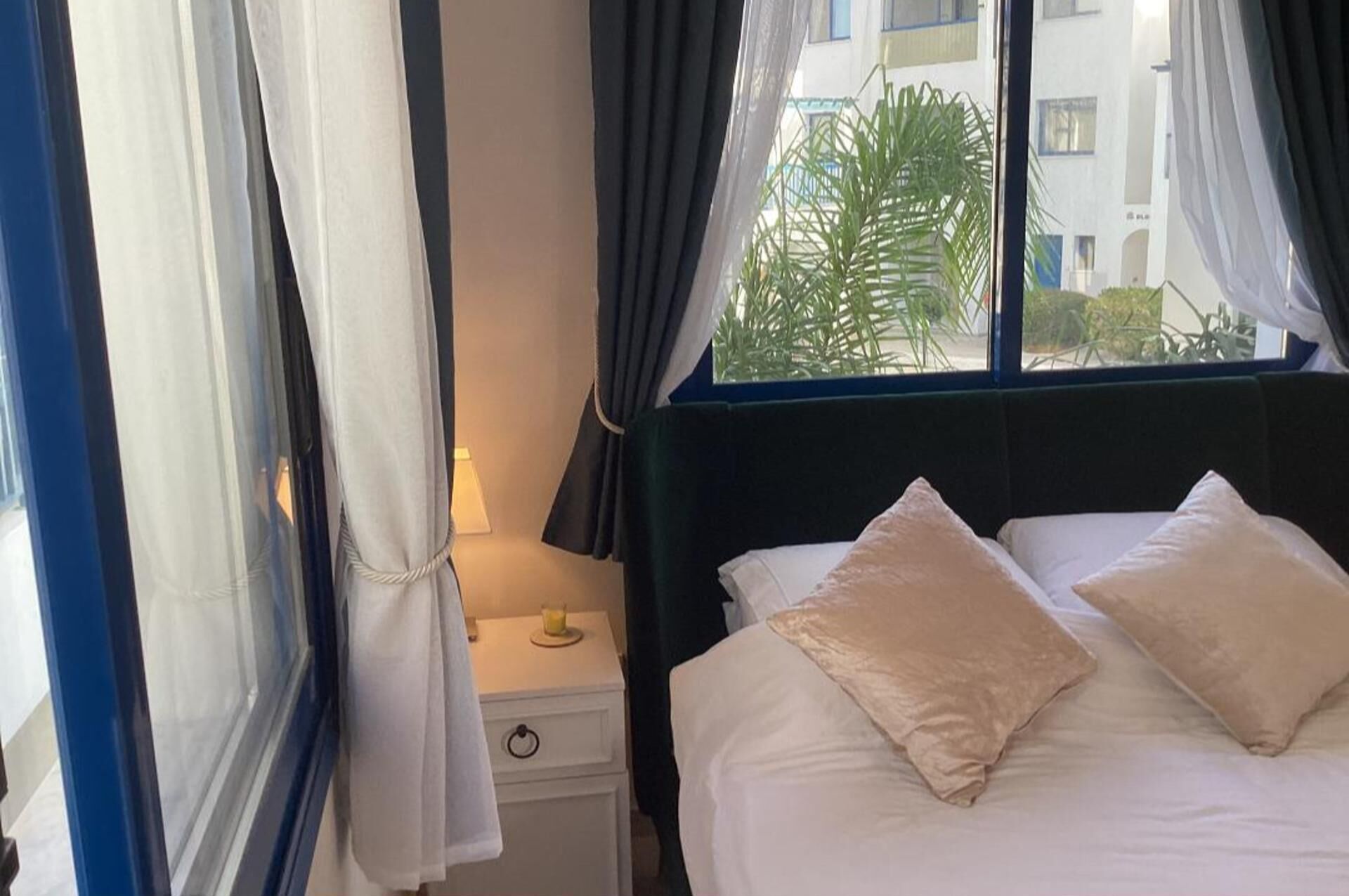 A hotel room with a bed, a nightstand, a lamp, and a window with curtains.