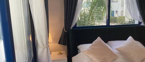 A hotel room with a bed, a nightstand, a lamp, and a window with curtains.