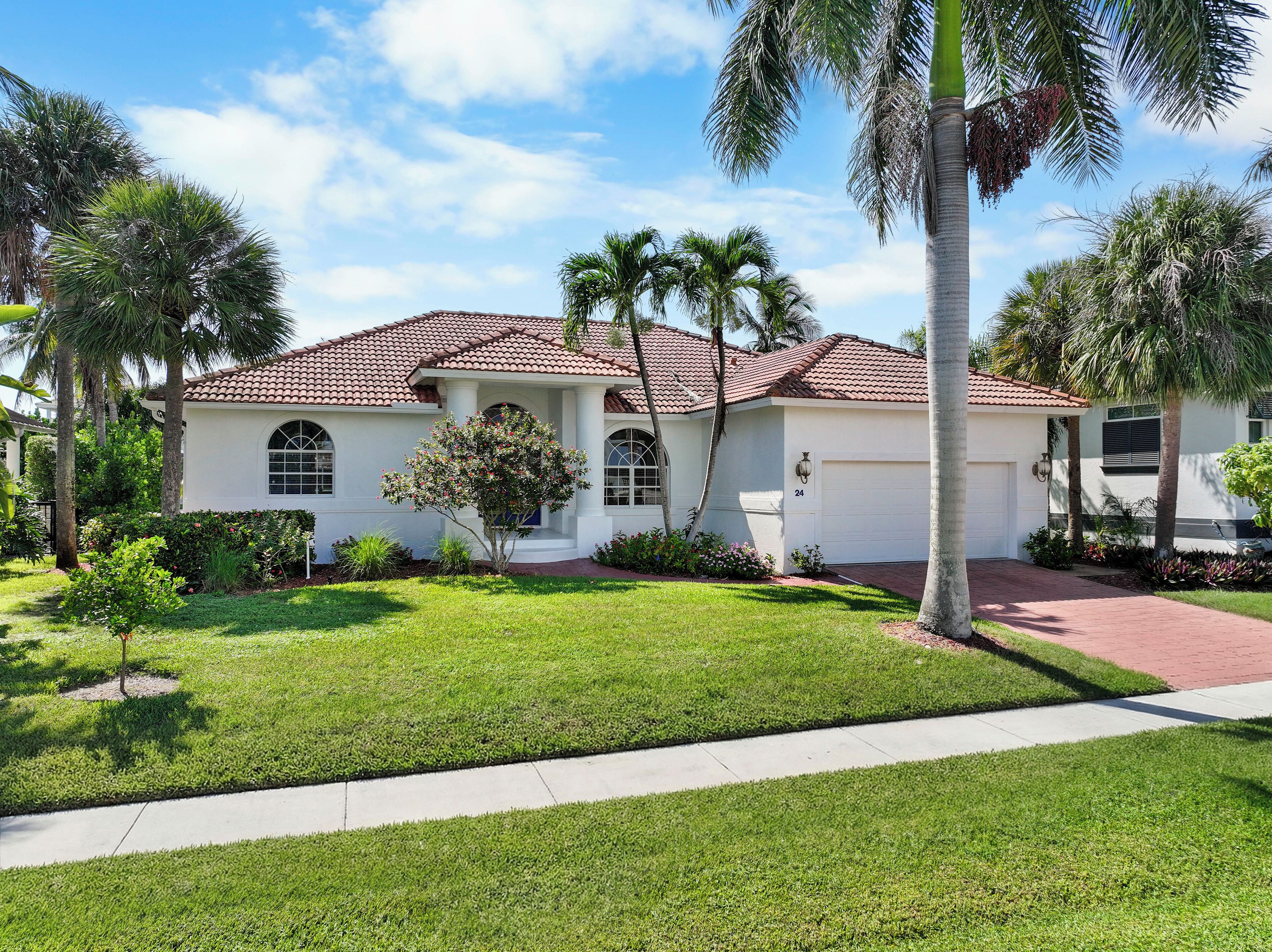 A single-story house with a red-tiled roof, a white exterior, and a well-maintained front yard with grass and palm trees.