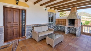 Un patio con chimenea de piedra, un sofá y una mesa de vidrio.