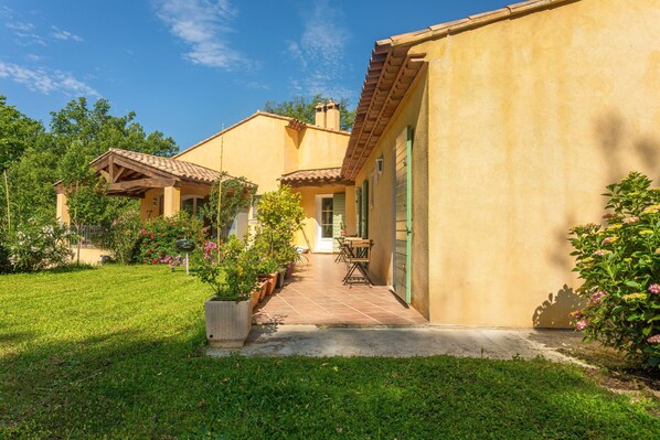 A two-story house with a patio, a small garden, and a door leading to the interior.
