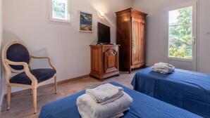 A room with two beds, a wooden cabinet, a chair, a television, and a window with a view of greenery. - "Azur" Room with Shared Pool, Wi-Fi, and Air Conditioning (Collobrières)