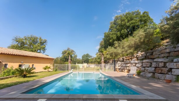 A rectangular swimming pool with a white fence, surrounded by a stone wall and a tiled roof building. - "Azur" Room with Shared Pool, Wi-Fi, and Air Conditioning (Collobrières)