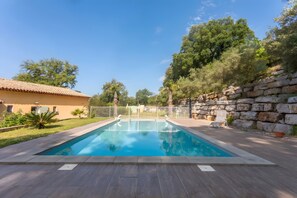 A rectangular swimming pool with a white fence, surrounded by a stone wall and a tiled roof building. - "Azur" Room with Shared Pool, Wi-Fi, and Air Conditioning (Collobrières)