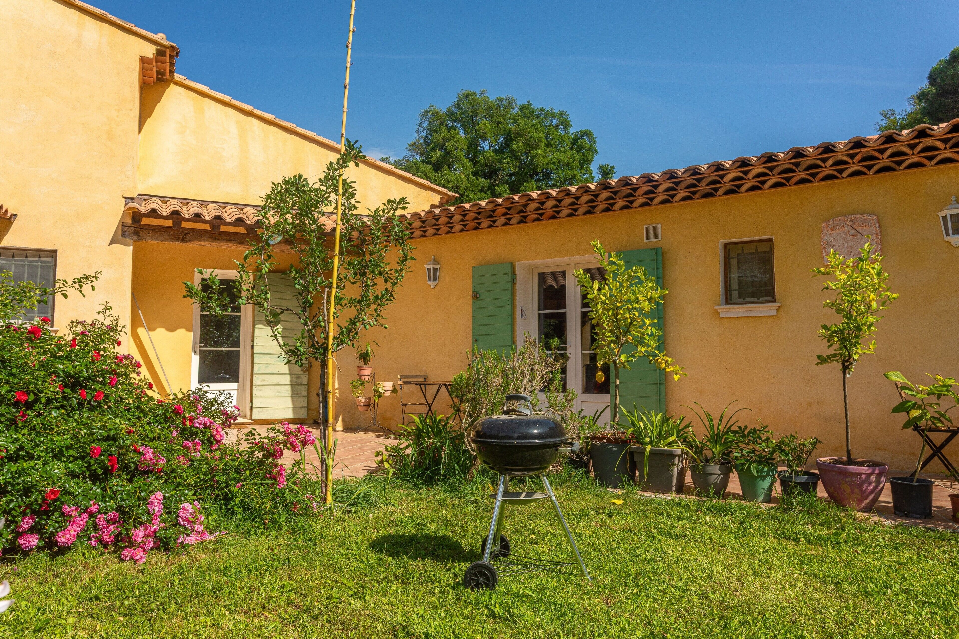 Un edificio giallo con tetto in tegole, una griglia per barbecue e piante in vaso.