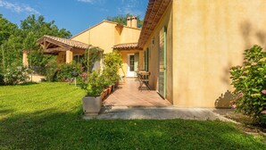 Une maison à deux étages avec un patio, un petit jardin et une porte donnant sur l’intérieur.