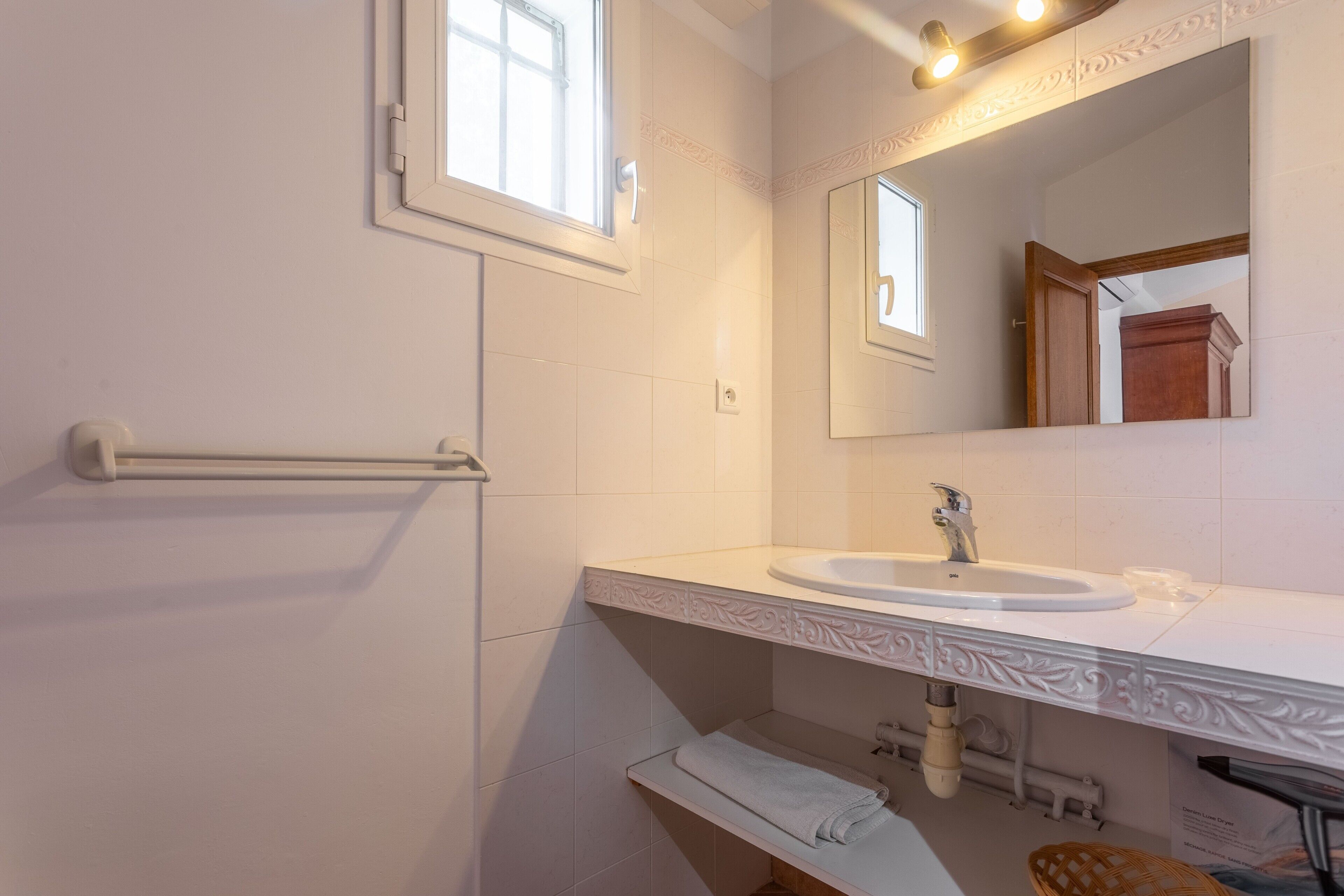 Une salle de bain avec un lavabo blanc, un porte-serviettes, un miroir et une fenêtre.